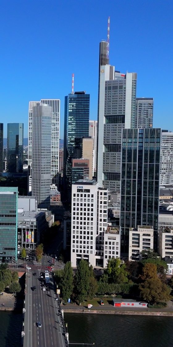 Ein grau-silberner Drohne fliegt vor einem blauen Himmel.