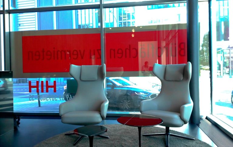 Zwei moderne weiße Sessel stehen vor großen Fenstern mit roter Beschriftung.