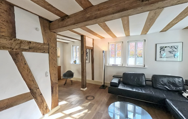 Moderne Wohnräume mit Holzbalken, schwarzem Sofa und runder Glastisch.